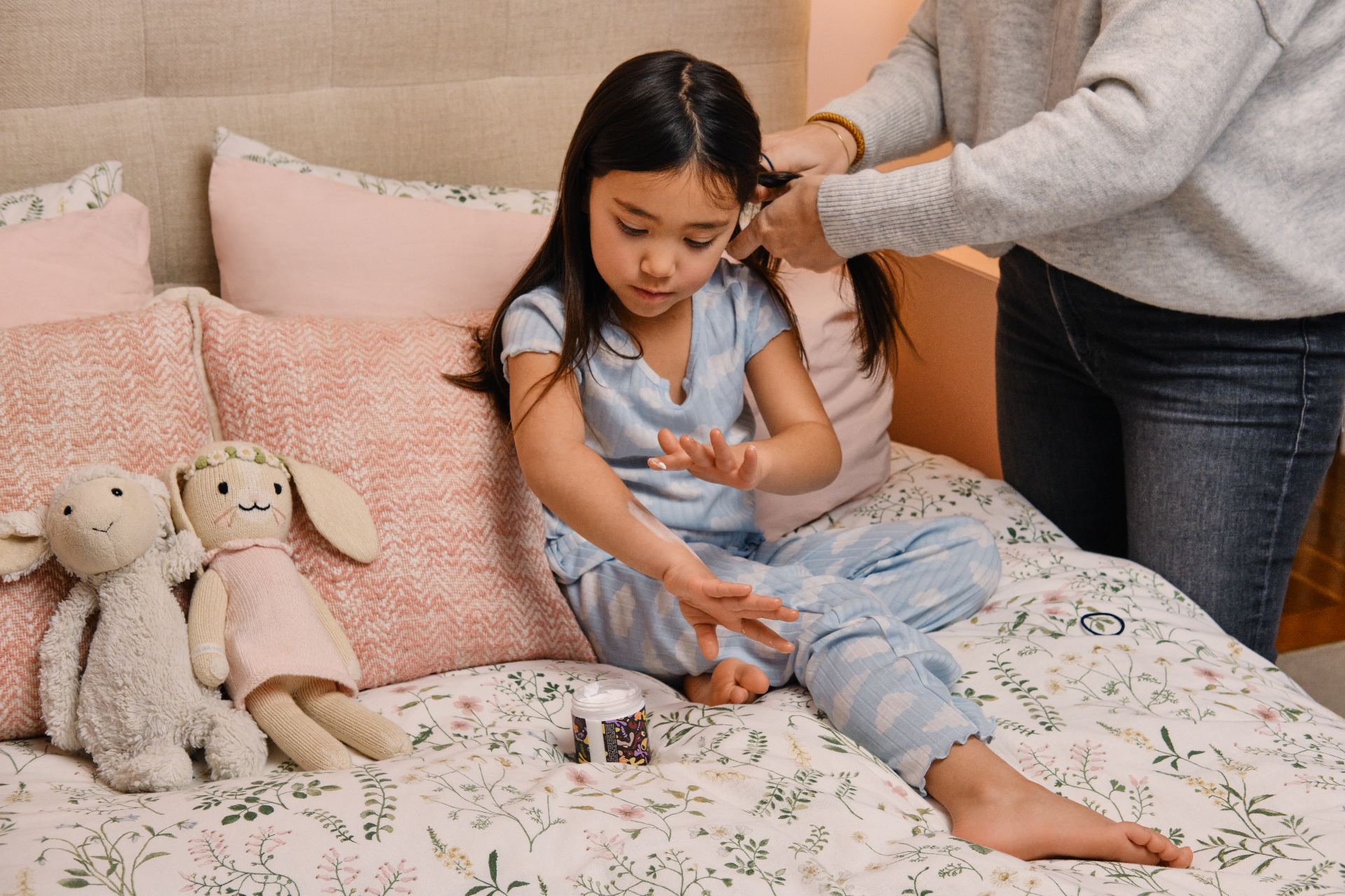 A parent braiding a child's hair while she rubs Good Dream Cream™ into her hands at bedtime